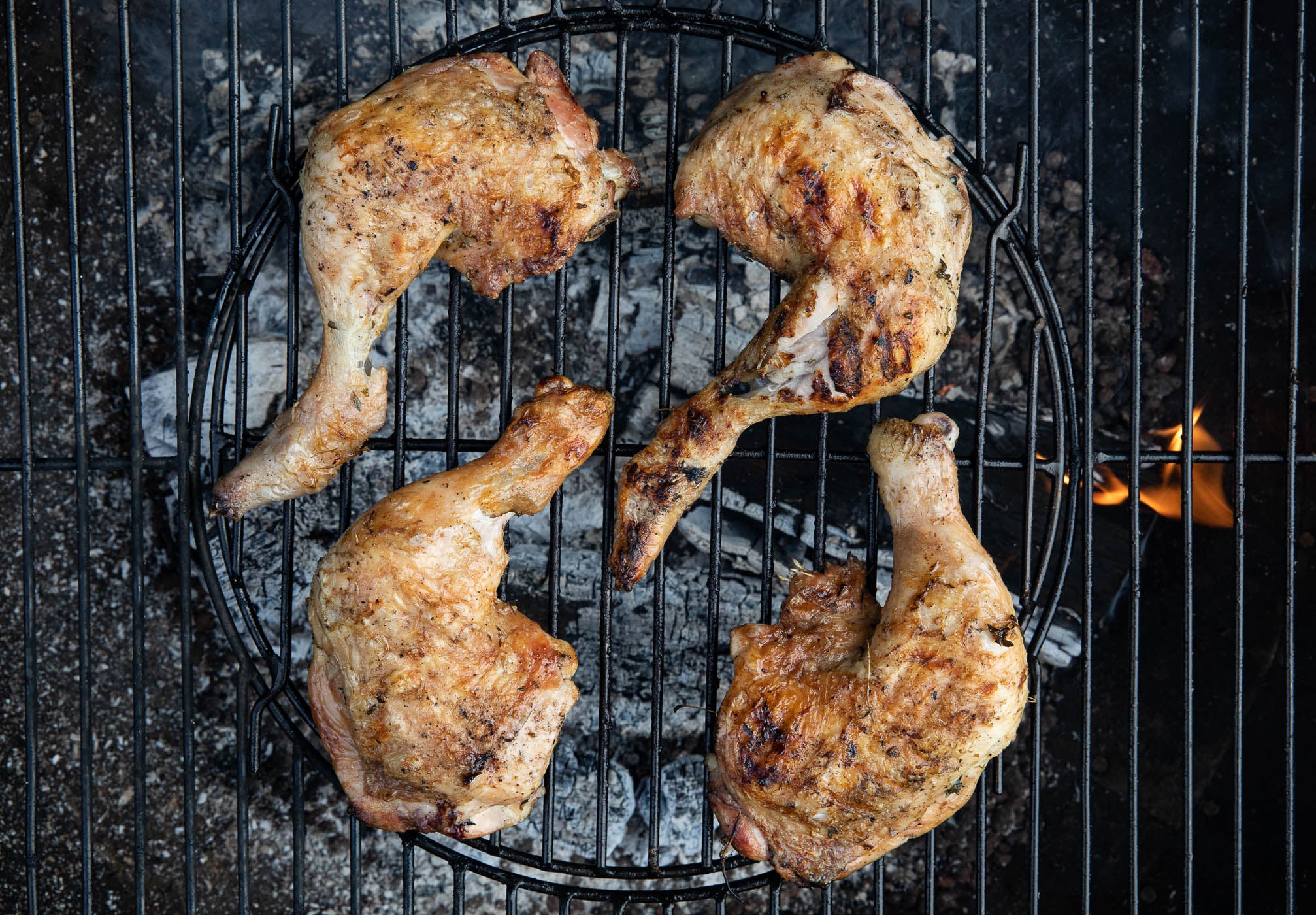 four skin-on chicken legs cooking on the barbecue