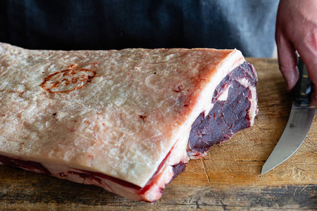 Raw whole grass-fed beef sirloin rack, bone-in, with fat cap, on a butcher’s block.